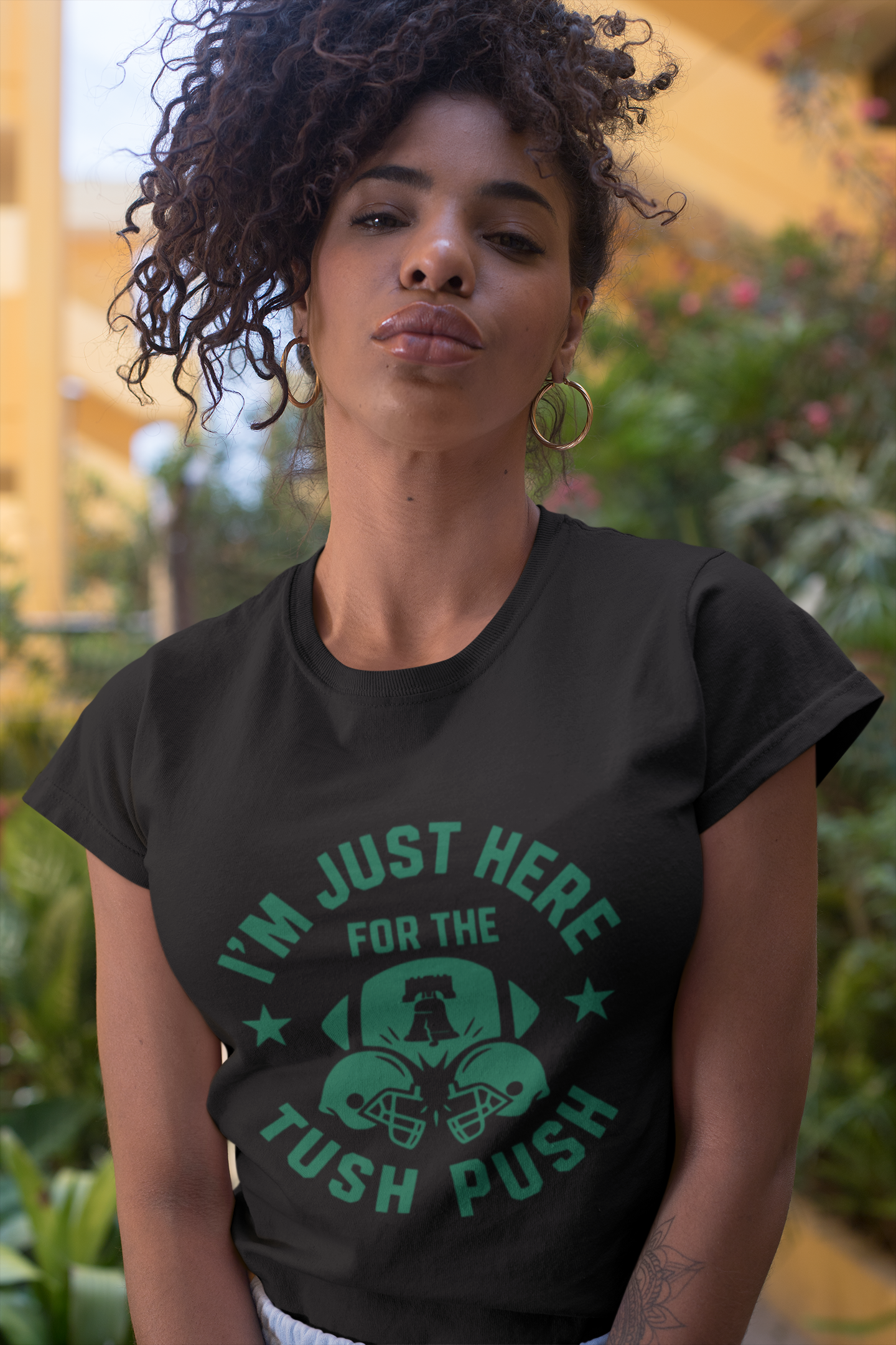Woman wearing a black tush push t-shirt with green text and graphics outdoors.