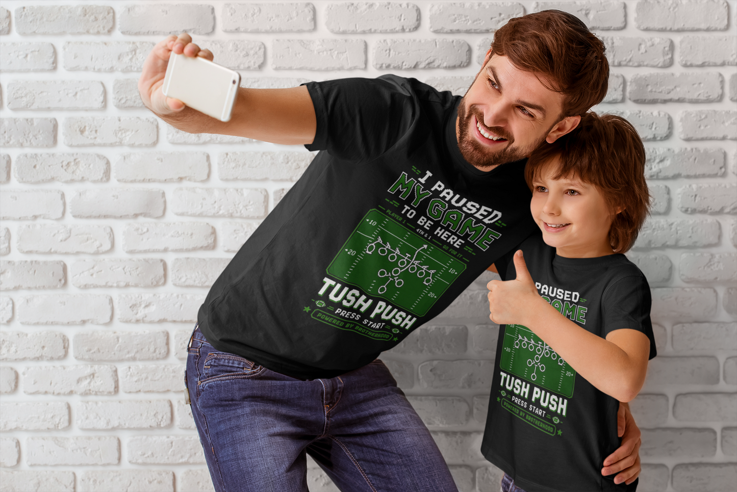 Man and child wearing matching t-shirts with humorous graphics and text against a brick wall.