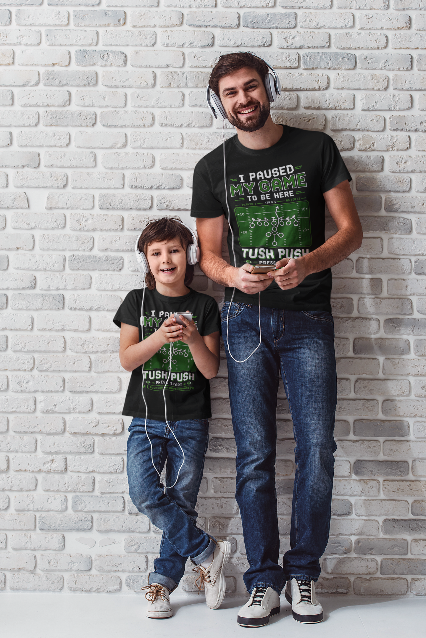 Two people wearing matching t-shirts with text standing against a light brick wall.
