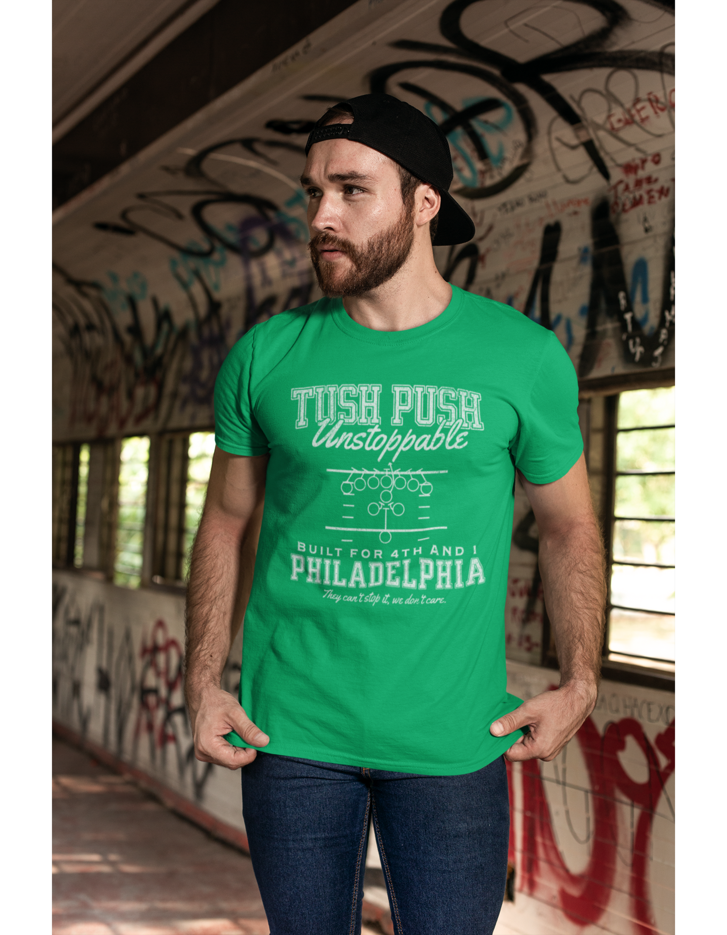 Man wearing a green t-shirt with Tush Push text and play diagram in an urban setting with graffiti.
